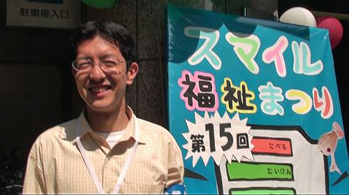 石坂わたるの活動：実行委員会事務局長として参加したスマイル福祉まつりの看板の前での写真